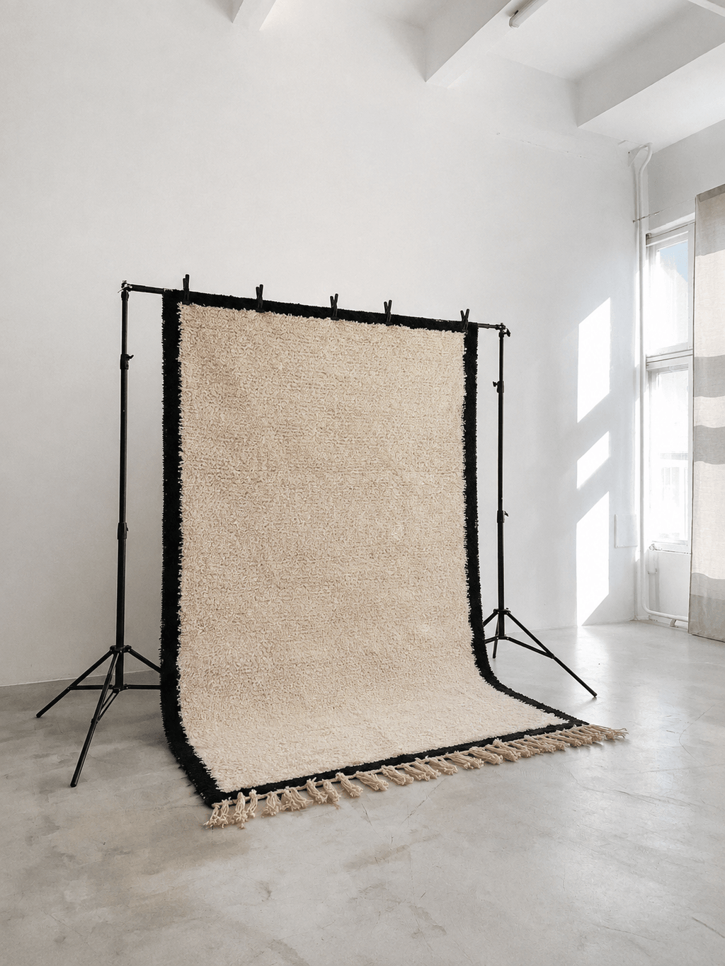 Handmade cream wool Moroccan Berber rug with black borders on a studio backdrop stand