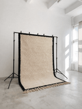 Handmade cream wool Moroccan Berber rug with black borders on a studio backdrop stand