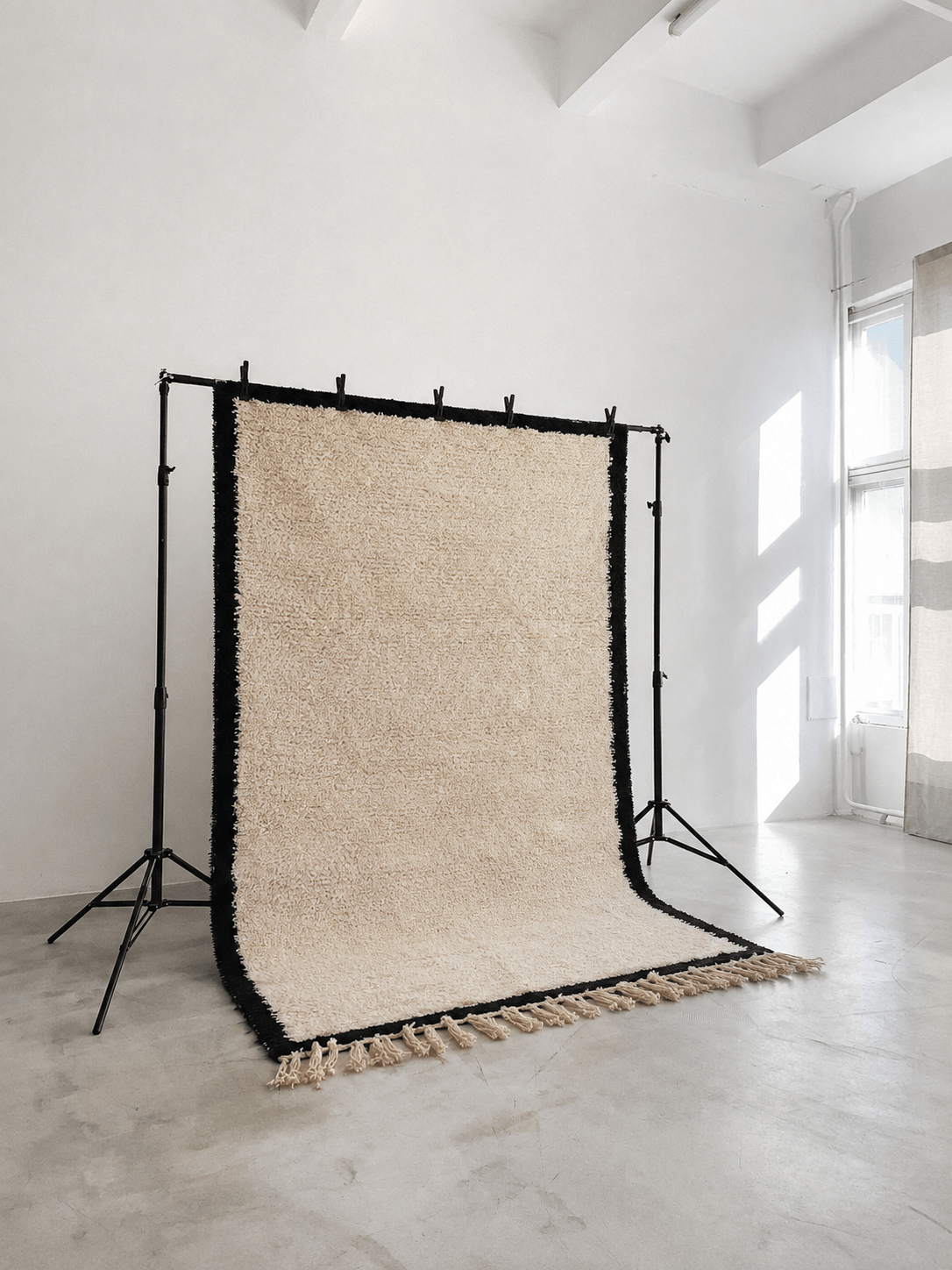 Handmade cream wool Moroccan Berber rug with black borders on a studio backdrop stand