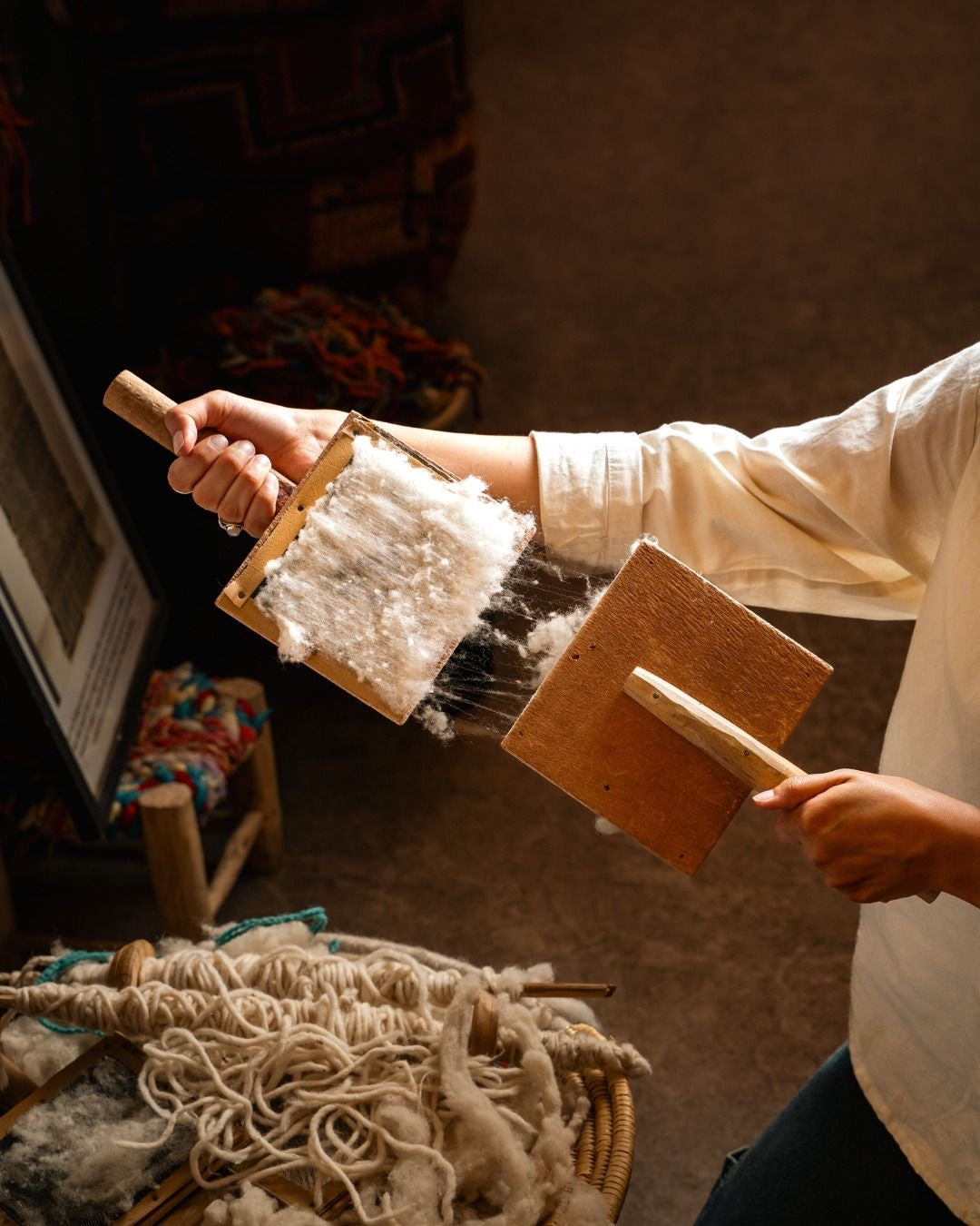 Artisan using a hand tool to card natural wool for a handmade Moroccan rug.