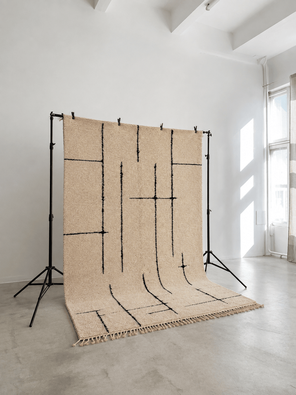 Handmade beige Moroccan Berber wool rug with minimalist black geometric lines on a display stand.