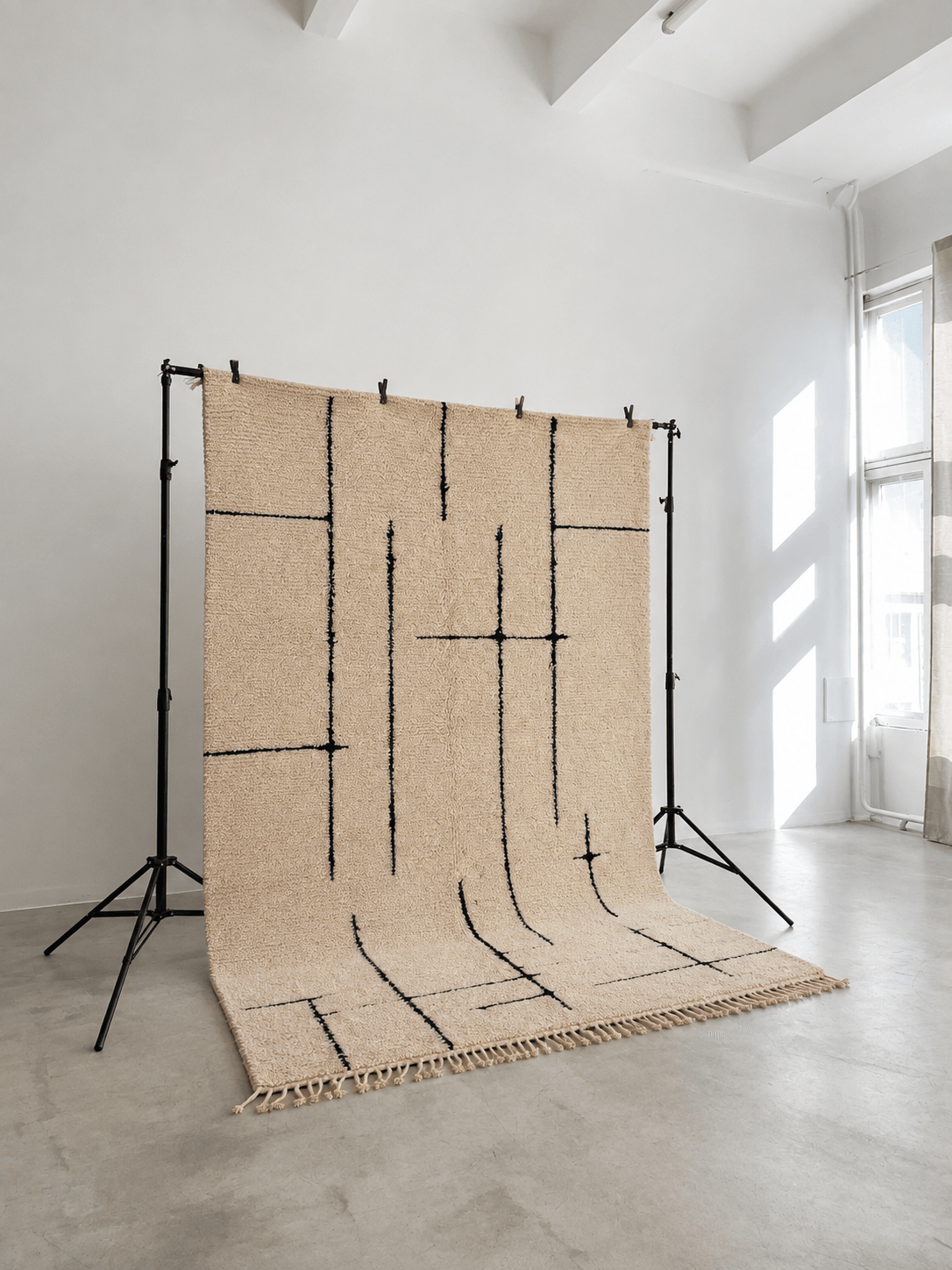 Handmade beige Moroccan Berber wool rug with minimalist black geometric lines on a display stand.