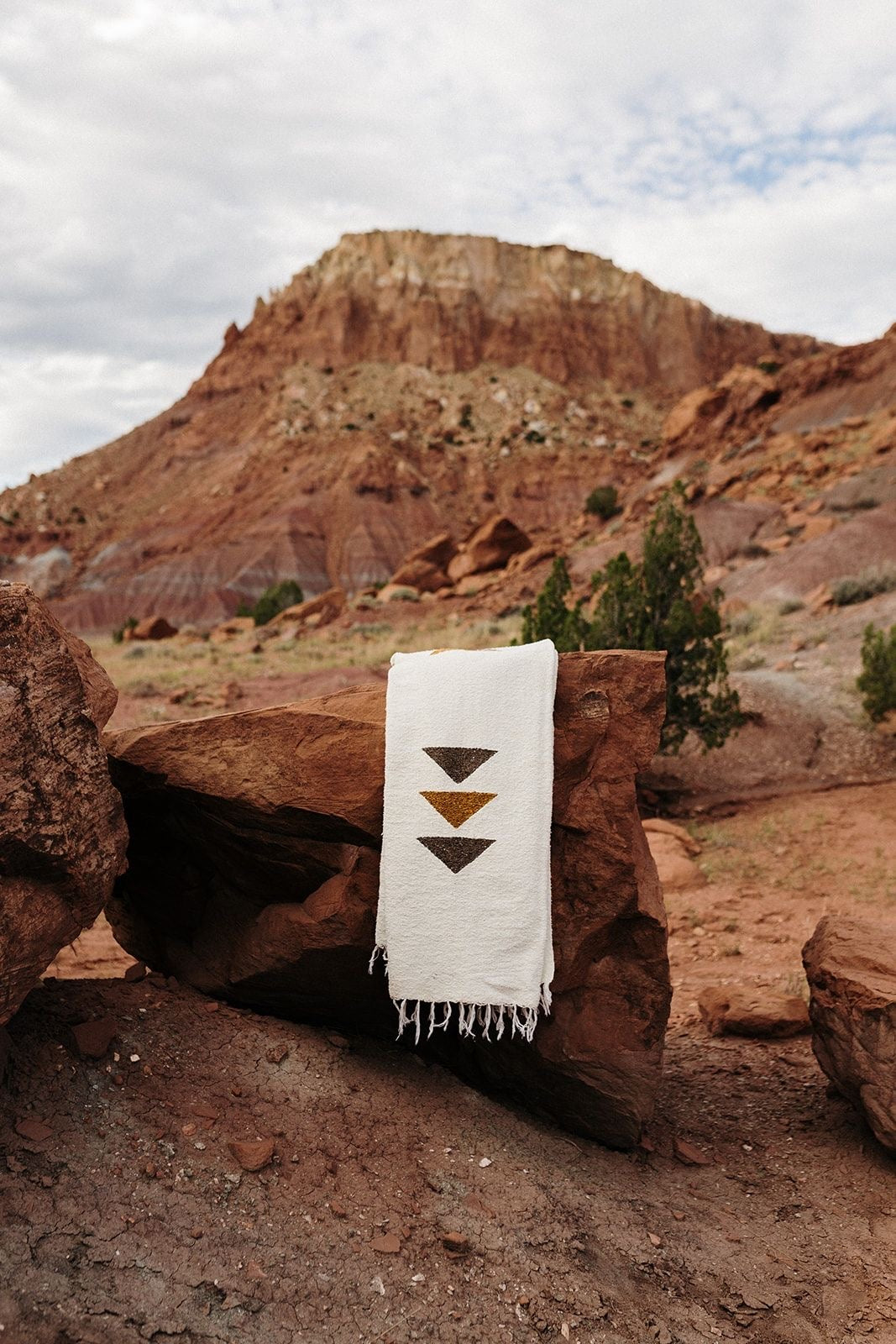 Handmade white wool Berber textile with brown geometric patterns draped over a red rock.